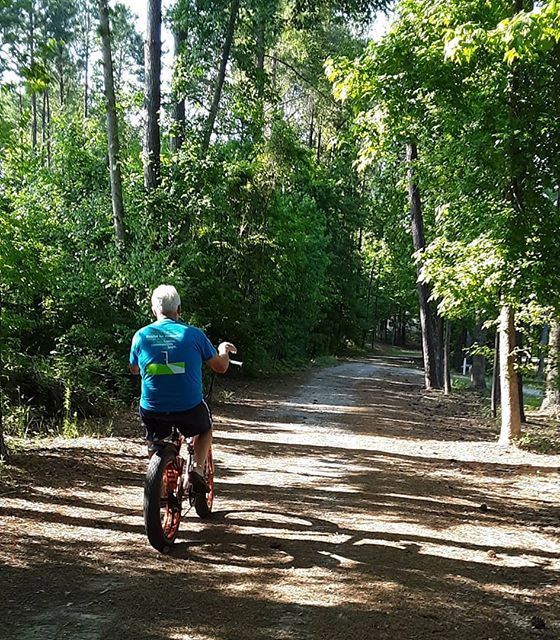 A guest riding a bike down a shaded dirt trail through the woods