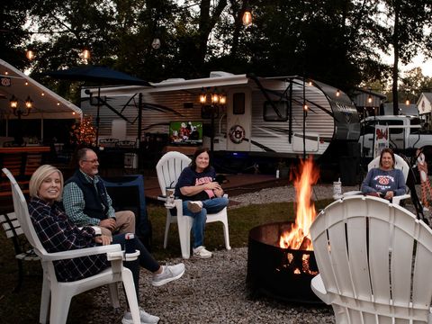 Guests in camp chairs around a fire pit at their RV site, with a rig behind them