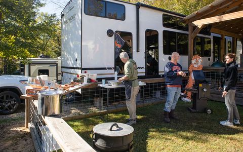 Guests cooking and talking at a tailgate beside an RV under a pavilion