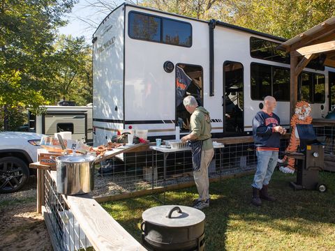 Guests cooking and talking at a tailgate beside an RV under a pavilion