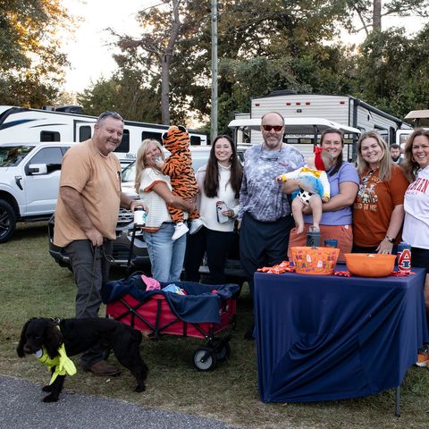 A group of friends and family gathered around a tailgate table beside their RV at University Station